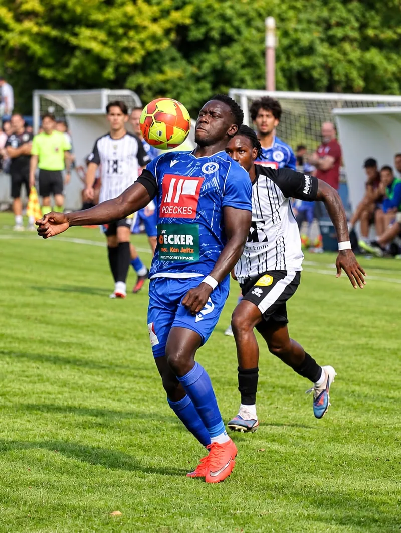 Futebol: jogador de equipamento azul domina a bola de peito, disputado por adversário de listras.